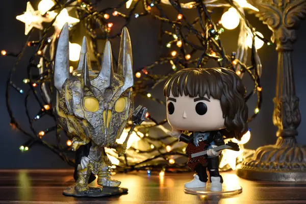 Yüzüklerin Efendisi filminden Funko Pop oyuncakları ve Yabancı Şeyler filminden Eddie. Turuncu ışıklandırma, siyah arkaplan, renkli çelenk, karanlık yer.
