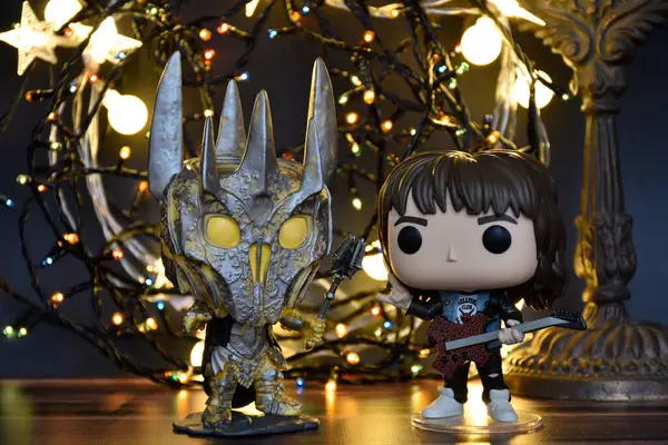 Yüzüklerin Efendisi filminden Funko Pop oyuncakları ve Yabancı Şeyler filminden Eddie. Turuncu ışıklandırma, siyah arkaplan, renkli çelenk, karanlık yer.