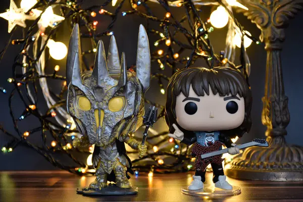 Yüzüklerin Efendisi filminden Funko Pop oyuncakları ve Yabancı Şeyler filminden Eddie. Turuncu ışıklandırma, siyah arkaplan, renkli çelenk, karanlık yer.