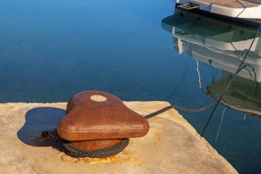 Güneşli bir günde iskeleye halatla bağlanmış eski bir demirleme kordonu. Demirli yat sakin suya yansıyor. Adriyatik Denizi, Karadağ. Boşluğu kopyala