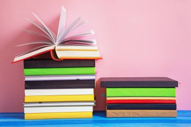 Kırsal masada iki renkli kitap yığını, bir kitap açık. Boşluğu kopyala