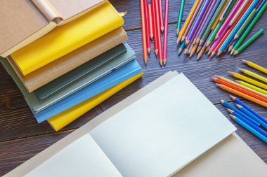 Kitap yığını, eskiz defteri ve kırsal masadaki renkli kalemler. Boşluğu kopyala