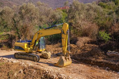 Dağlarda yeni yol inşaatı. Sarı çizgili kazıcı, yolun seviyesini yükseltmek için kovasını kullanıyor. Karadağ, Dinariç Alpleri, Tivat