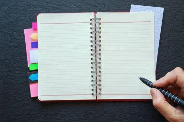 Karanlık masa üzerinde parlak yer imleri olan sarmal defter. Boş bir sayfanın üzerinde kalemle. Not defterine odaklan. Düz yat, boşluğu kopyala