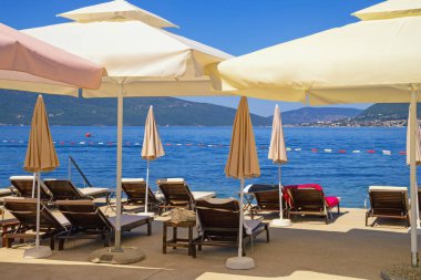 Yaz tatili. Karadağ, Adriyatik Denizi, Kotor Körfezi. Tivat şehri yakınlarındaki sahil, şezlonglar ve plaj şemsiyeleri.