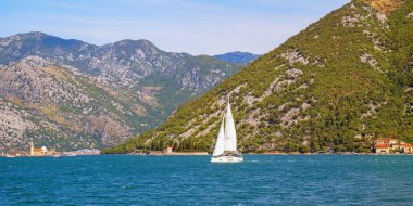 Beautiful autumn Mediterranean landscape. Montenegro, Adriatic Sea. View of coast of Bay of Kotor near Perast town. Sailboat with white sail on water. Vacations and recreation concept