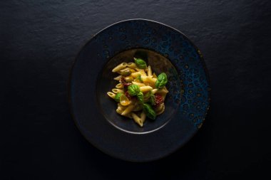 Arka planda domates ve fesleğenli makarna tabağı.