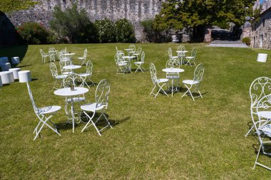 Çimlere dizilmiş beyaz metal masalar ve sandalyeler.