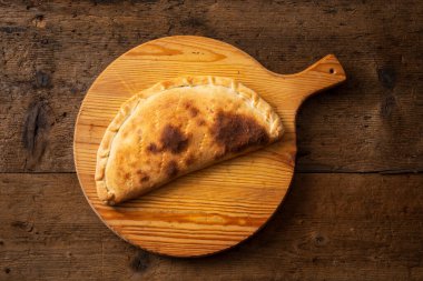 Kesme tahtasında üst görünüm calzone, İtalyan gastronomik uzmanlık alanı, ahşap arka plan