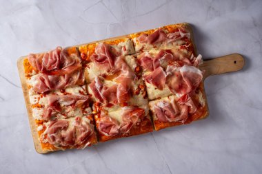 Tavada pizza, ahşap kesim tahtasında jambon.