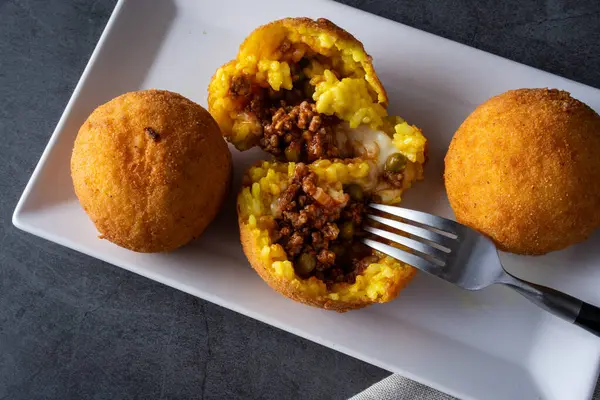 Koyu arkaplanda açık arancini plakası var. İtalyan pirinç topları.