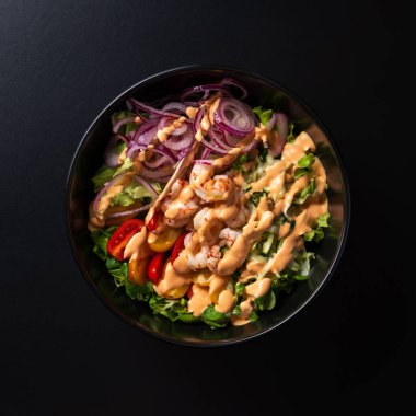 Üst tabakta karışık salata ve siyah arka planda karides var.