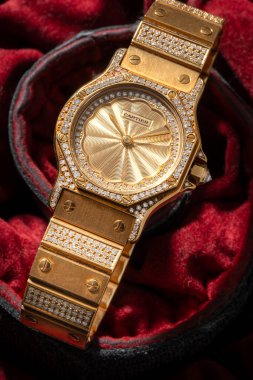 Cartier saat, Santos Bayan Evren modeli. Otomatik saat, sarı altın çanta, kırmızı kumaş arka planda 2965 'ten bahsediyor. Milan mı? İtalya _ 12 Kasım _ 2024