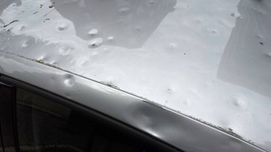 Dolu yüzünden ağır hasar gören bir arabanın çatısı. Fırtınanın etkisiyle oluşan çok sayıda görünür göçük var..