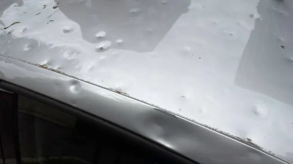 Dolu yüzünden ağır hasar gören bir arabanın çatısı. Fırtınanın etkisiyle oluşan çok sayıda görünür göçük var..