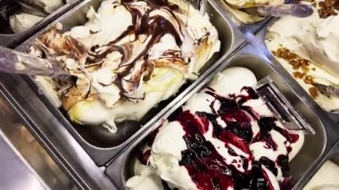 Tezgahın arkasında çeşitli aromalı sanatsal dondurma küvetleri var. Bir dondurma üreticisi bir külah hazırlıyor.