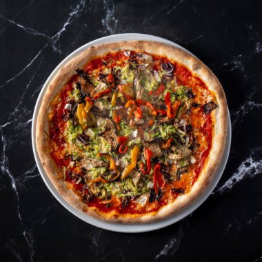 Siyah mermer bir yüzey üzerinde duran bir tabak sebze pizzasının genel görüntüsü. Lezzetli ve renkli bir İtalyan yemeği sunumu.