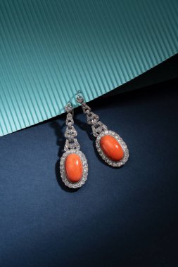 Parlak kesilmiş elmaslarla çevrili iki mercan damlasından oluşan zarif platin küpeler. Mavi bir arkaplanda fotoğraflandı.