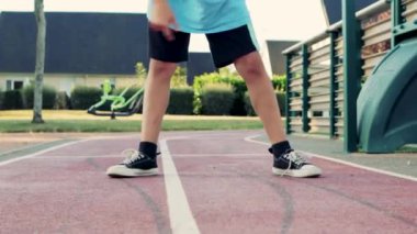 a boy of European appearance with blond hair in sportswear kicks a basketball on the court. High quality 4k footage