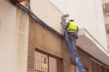 Yansıtıcı yelek giyen bir adam merdiven üzerinde elektrikle uğraşıyor. İş elbiseli bir adam evde kabloyu tamir eder. Yüksek kalite fotoğraf