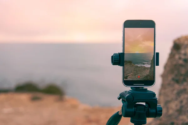 stock image  has a place for an inscription close-up on the phone,smartphone camera stands on a tripod close-up, photographing a picturesque evening sunset over a tropical sea and a mountain. High quality photo