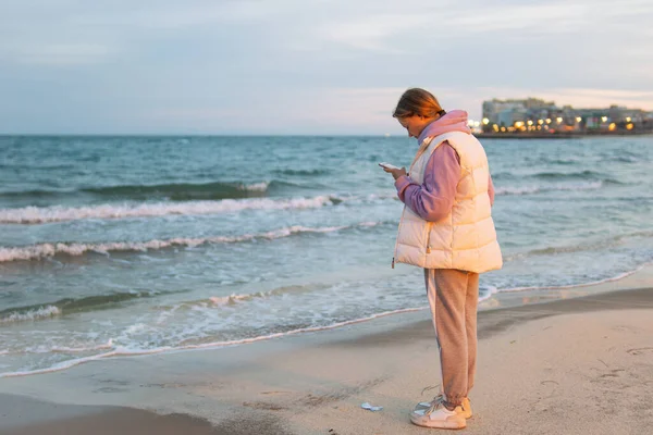 Avrupai Giysili Bir Kız Elinde Telefonla Okyanusun Kenarında Dikiliyor Telefona — Stok fotoğraf