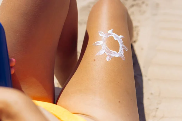 Beautiful tanned female legs on the beach, close-up, the sun is drawn on the leg with white sunscreen. High quality photo
