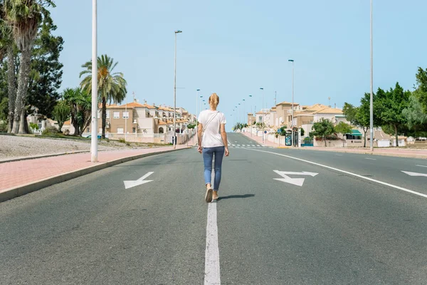 Tişörtlü ve kot pantolonlu bir Avrupalı kız kameraya arkası dönük bir şekilde yol boyunca yürüyor, bir kızla güzel bir şehir manzarası. Yüksek kalite fotoğraf