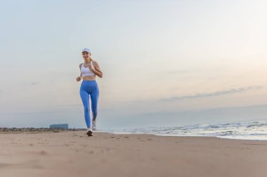 Güzel, sportif bir kadın kumlu sahilde koşuyor, sağlıklı bir hayat sürüyor, deniz kenarında aktif bir yaz tatilinin tadını çıkarıyor. Yüksek kalite fotoğraf