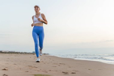 Güzel, sportif bir kadın kumlu sahilde koşuyor, sağlıklı bir hayat sürüyor, deniz kenarında aktif bir yaz tatilinin tadını çıkarıyor. Yüksek kalite fotoğraf