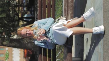 VERTICAL VIDEO, genç kadın park bankında oturuyor, cep telefonu kullanıyor. Yüksek kaliteli FullHD görüntüler