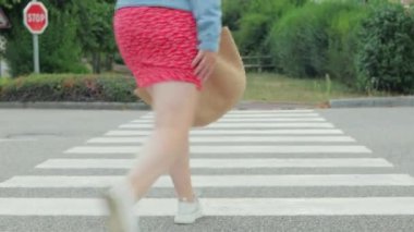 Kırmızı elbiseli ve kot ceketli bir kadın yaya geçidinden atlıyor. Sırtı kameraya dönük. Yüksek kalite 4k görüntü