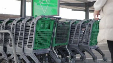 Marketin yakınındaki el arabalarının yakınında, günlük kıyafetleri olan bir kız market arabasını alır. Yüksek kalite 4k görüntü