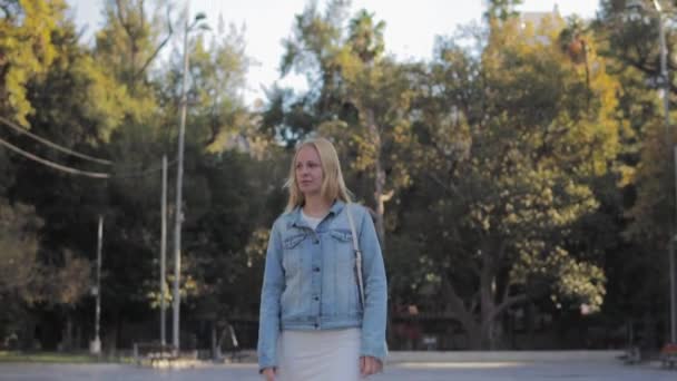 Дівчина Білій Сукні Джинсова Куртка Сумочкою Плечі Проходить Через Парк — стокове відео