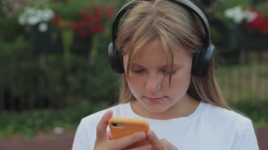 Şehrin arka planında duran siyah kulaklıklı ve akıllı telefon kullanan genç ve güzel bir kız. Bir kız telefonundaki bir konum uygulamasına bakıyor. Yüksek kalite 4k görüntü