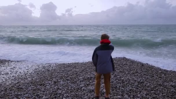 Ceketli Neşeli Genç Çocuk Okyanus Kıyısında Çakıl Taşlarının Üzerinde Duruyor — Stok video