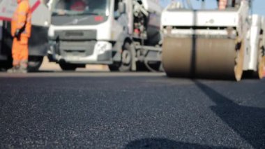 Yeni yerleştirilmiş bir asfalt tabakası. Yol yüzeyi tamiri. Yeni bir yol inşaatı. Patenler asfaltı düzleştirip sıkıştırıyor. Yol silindirleri. Güneş parlıyor. Yüksek kaliteli FullHD görüntüler