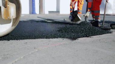 Koruyucu giysiler içindeki yol işçileri, asfalt yüzeyini sıcak asfalt ile onarıyor, işçilerin ayaklarına yakın çekim, yavaş çekim. Yüksek kaliteli FullHD görüntüler