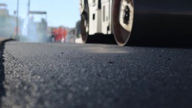 Güneşe yeni bırakılmış bir asfalt tabakası. Yol yüzeyi tamiri. Yeni bir yol inşaatı. Patenler asfaltı düzleştirip sıkıştırıyor. Yol silindirleri. Güneş parlıyor. Yüksek kaliteli FullHD görüntüler