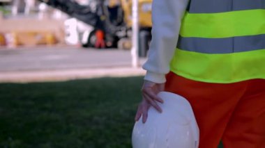 Bir kız mühendis, sırtını kameraya dayamış, elinde beyaz bir miğfer tutan bir kız, insanların çalışma sürecini, yol onarımı kavramını izliyor. Yüksek kaliteli FullHD görüntüler