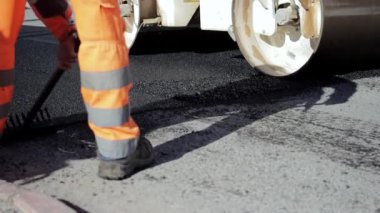 Bir grup işçi yol boyunca caddeye sıcak asfalt bırakıyor. Buharlı silindir. Koruyucu üniformalı kürekçiler. Sıcak bir günde çalışmak. Yüksek kaliteli FullHD görüntüler