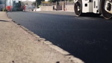 Batan güneşin ışınlarında yeni serpilmiş bir asfalt tabakası. Yol yüzeyi tamiri. Yeni bir yol inşaatı. Tekerlekler asfaltı düzleştirir ve sıkıştırır. Yol silindirleri. Yüksek kaliteli FullHD görüntüler