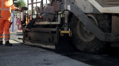 Asfalt kaldırım taşı taze sıcak asfalt karışımını yakın çekim yapar. Yakınlarda bir işçi işi yakından izler. Yüksek kaliteli FullHD görüntüler