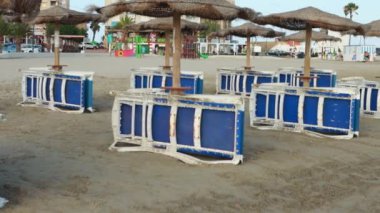 Boş plaj, İspanya 'da sabahın erken saatlerinde şemsiyelere bağlanmış katlanmış boş plaj sandalyeleri. İtalya ya da Yunanistan. Seyahat ve tatil kavramları. Yüksek kalite 4k görüntü
