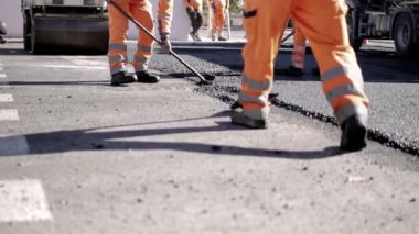 Bir grup işçi yol boyunca caddeye sıcak asfalt bırakıyor. Buharlı silindir. Koruyucu üniformalı kürekçiler. Sıcak bir günde çalışmak. Yüksek kaliteli FullHD görüntüler