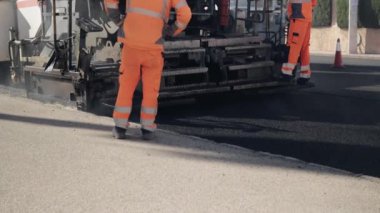  Yol tamiri. Bir yol makinesi caddeye asfalt serer. Bir grup işçi şehirde yol onarımı çalışması yapıyor. Yüksek kaliteli FullHD görüntüleri.