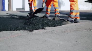 Koruyucu giysiler içindeki yol işçileri, asfalt yüzeyini sıcak asfalt ile onarıyor, işçilerin ayaklarına yakın çekim, yavaş çekim. Yüksek kaliteli FullHD görüntüler
