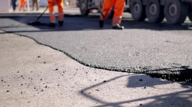 Yol inşaatında çalışan inşaat işçileri. Ağır çekimde. Sıcak asfalt yüzeyinden buhar yükseliyor. Bir işçi inşaat alanında yeni asfalt döşemiş. Yüksek kaliteli FullHD görüntüler