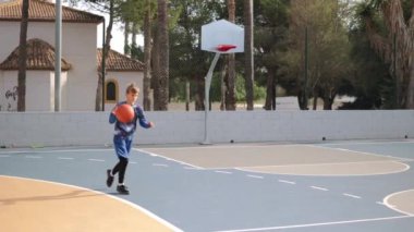  Basketbol sahasının arka planında top atan çocuk. Dışarıda basketbol antrenmanı yapan genç bir çocuk. Spor aktiviteleri ve mutlu çocukluk kavramı, yüksek kaliteli FullHD görüntüleri