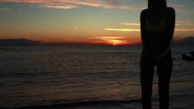 Deniz kıyısındaki ince bir kızın silueti güzel bir gün batımının arka planında dalgalarla birlikte. Yüksek kalite 4k görüntü